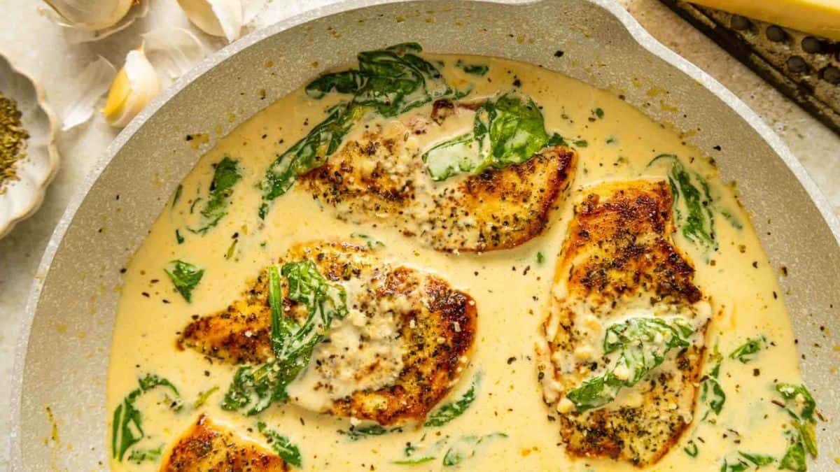 A pan with chicken drenched in creams sauce and spinach.