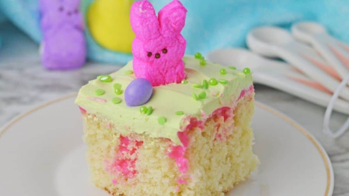 A single slice of easter poke cake, with topped with a bunny mallows, sitting on a ceramic plate. 
