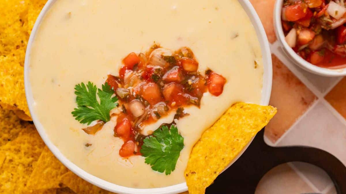 A close-up shot of a bowl filled with White Queso Dip, a nacho dipped in.