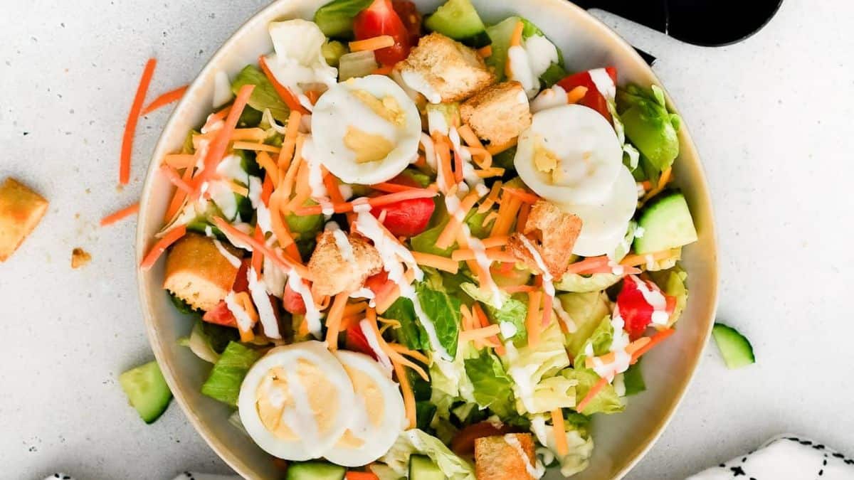 A top shot of a bowl filled with salad consists of lettuce, carrots slices, egg slices, some tomato slices. 