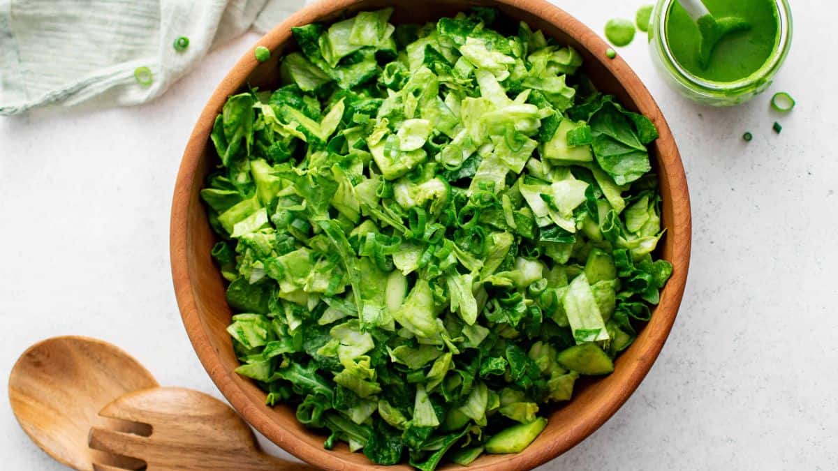 A top shot of a wooden bowl filled with Green Goddess Salad made with number of chopped greens, 