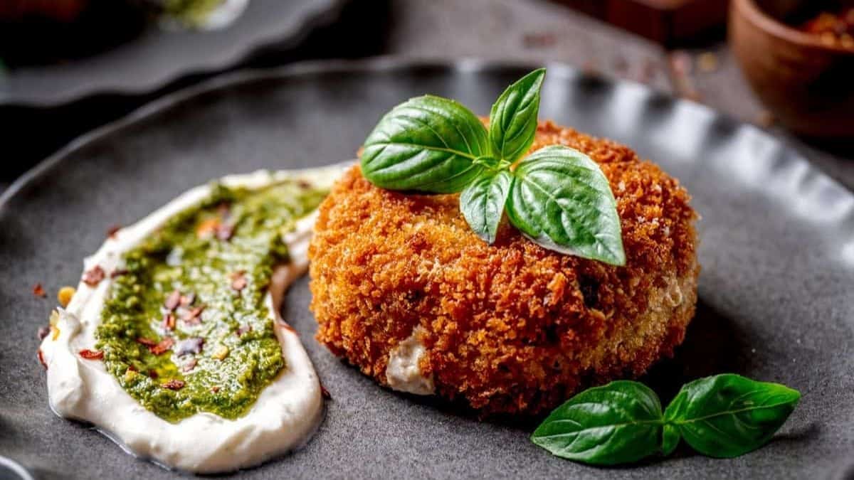A black plate with a pan-fried risotto cake and a swipe of sauce on its side. 