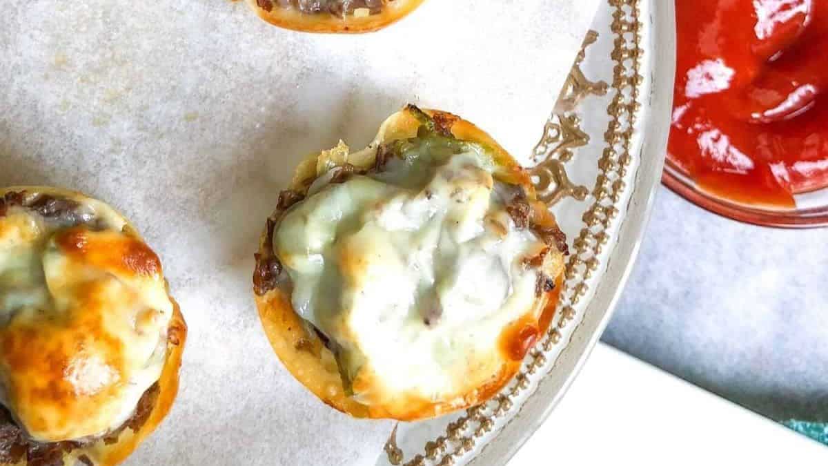 A couple of pieces of Philly Cheesesteak Wonton Cup set on a plate, a dip on the side. 