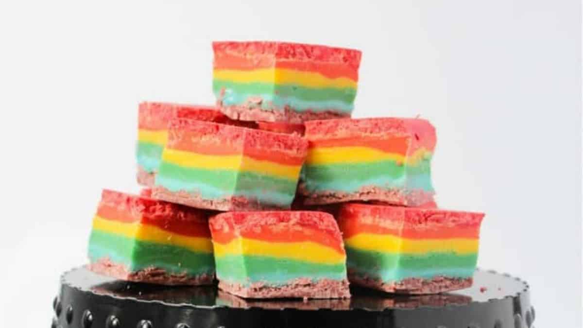 Rainbow fudges piled up while sitting on a dessert stand. 
