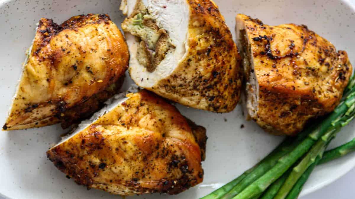 Four pieces of chicken breasts with stuffing and some asparagus on the side.