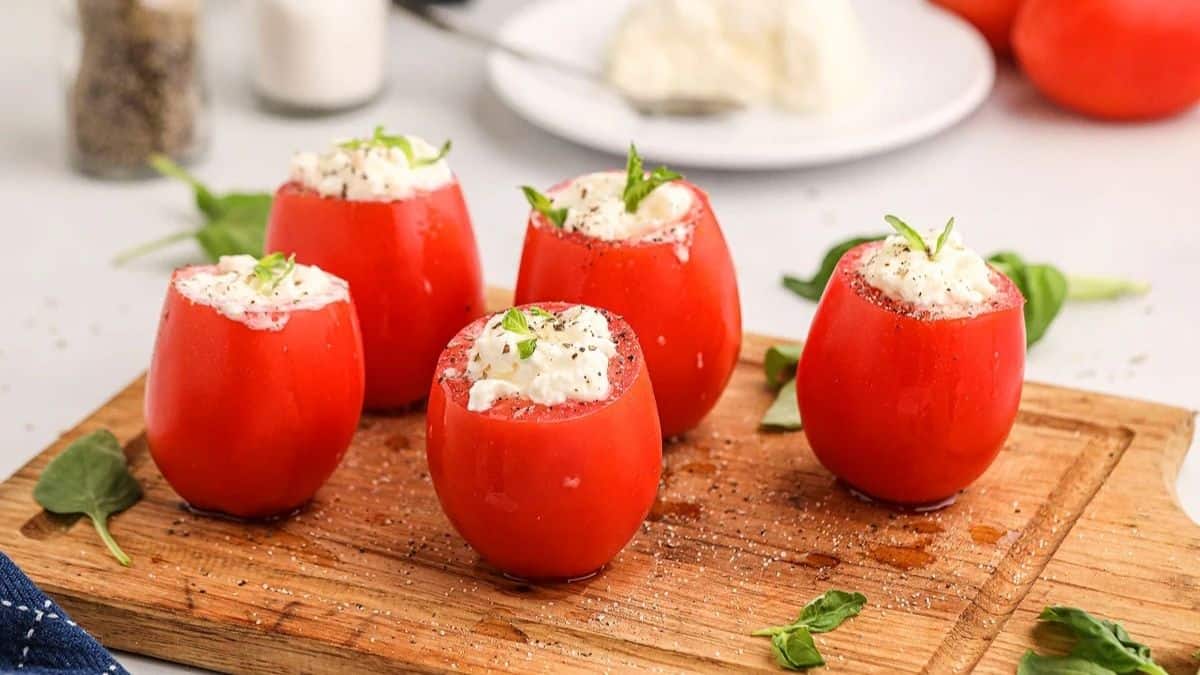 Five pieces if Tomatoes Burrata Bites sitting on a wooden board.
