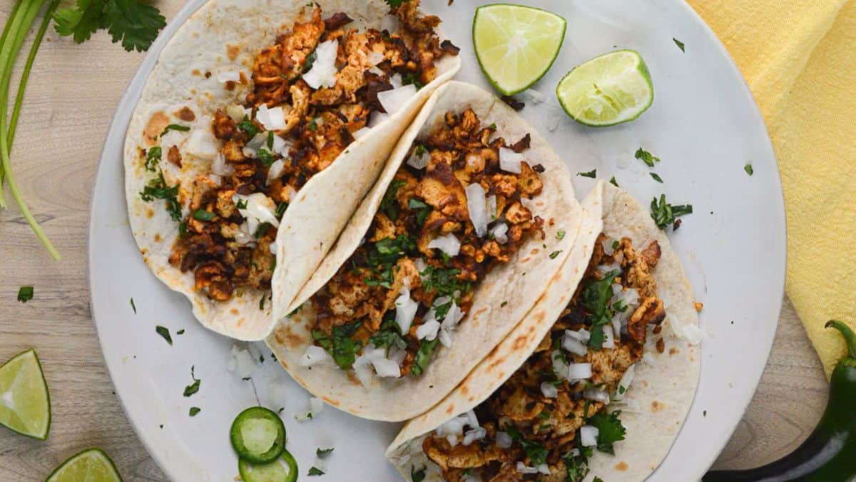 Top-shot of three pieces of vegan carnitas set on a plate, and a couple of wedges of lime. 