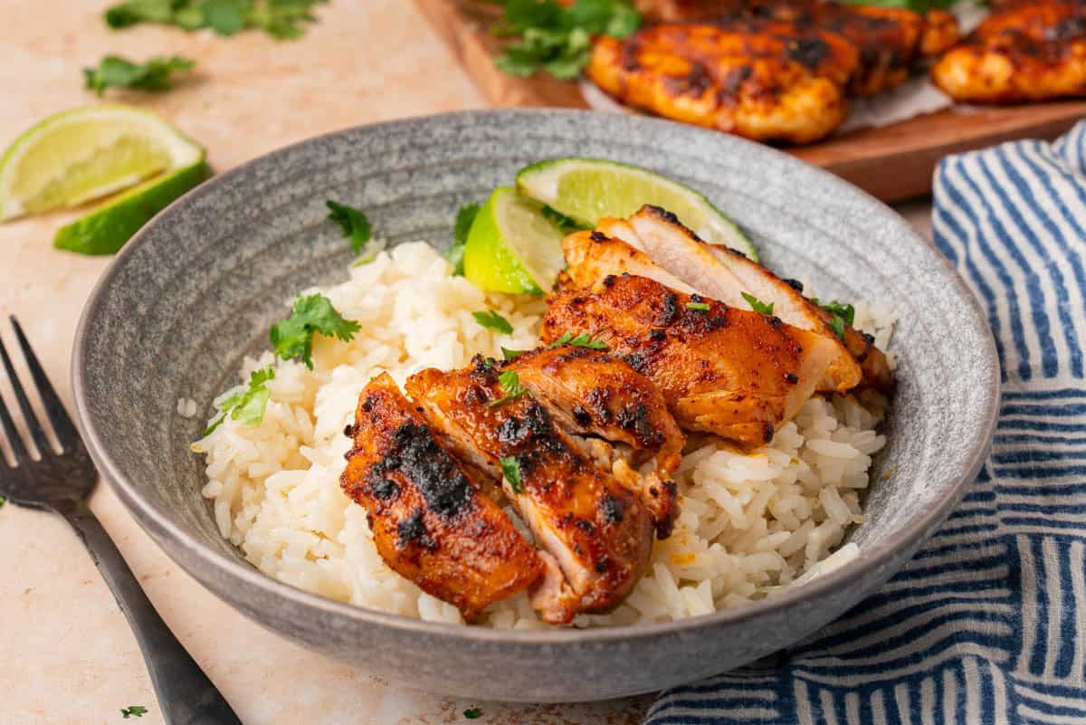 Close up shot of the chicken thighs in a bowl with rice, limes and cilantro. 