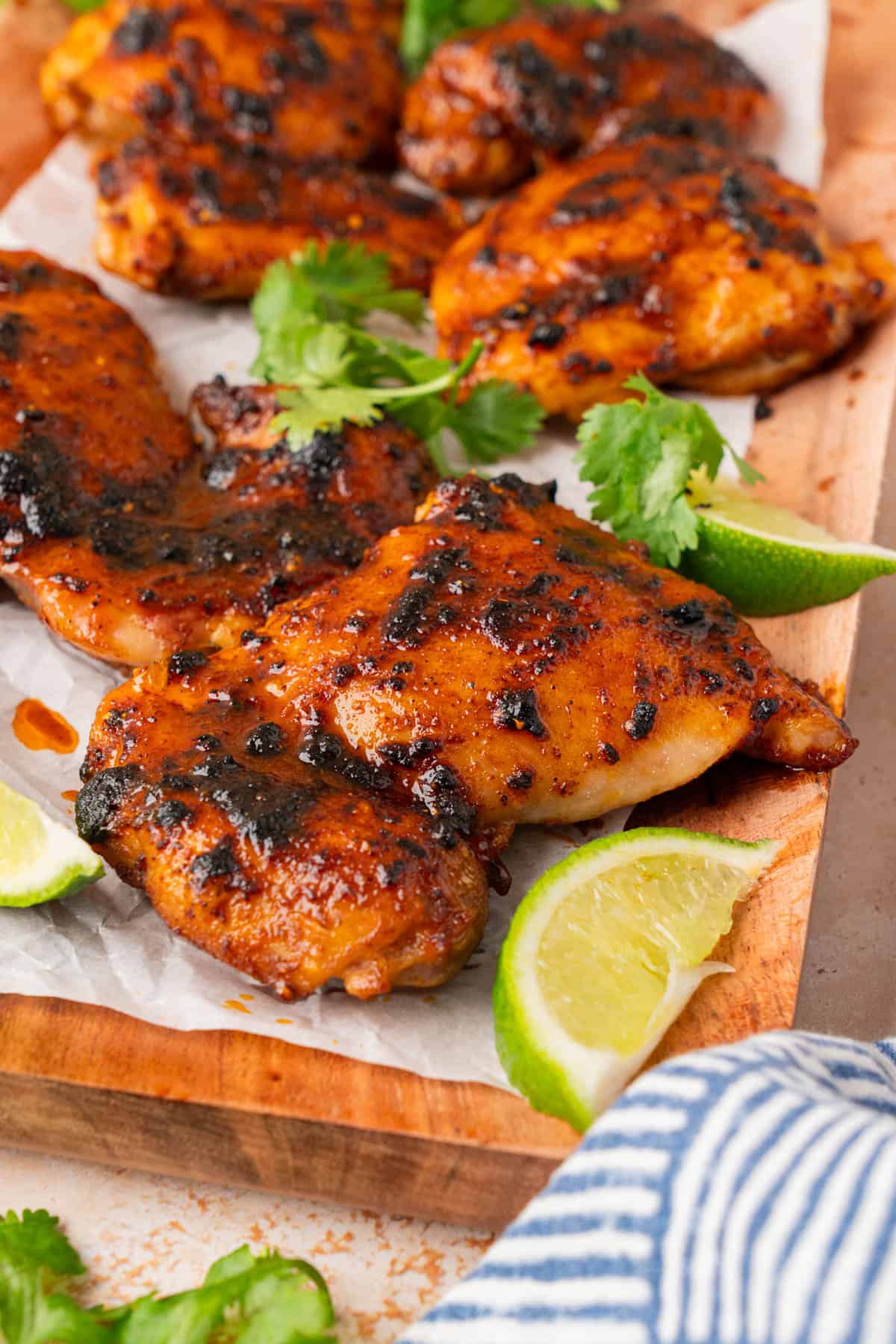 Close up shot of the chicken thighs on a wooden cutting board with limes and cilantro.