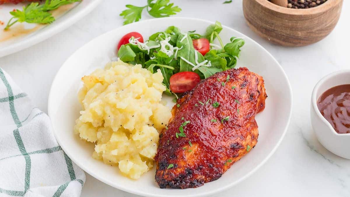 A plate with mashed potato, side salad, and a single piece of breast piece BBQ Chicken. 