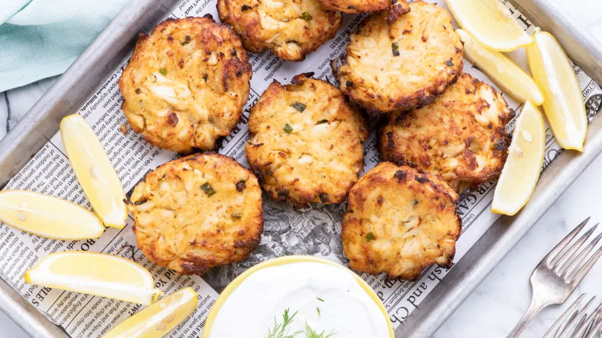 A couple pf pieces of crab cakes with a few pieces of lemon wedges and a dip on the side. 