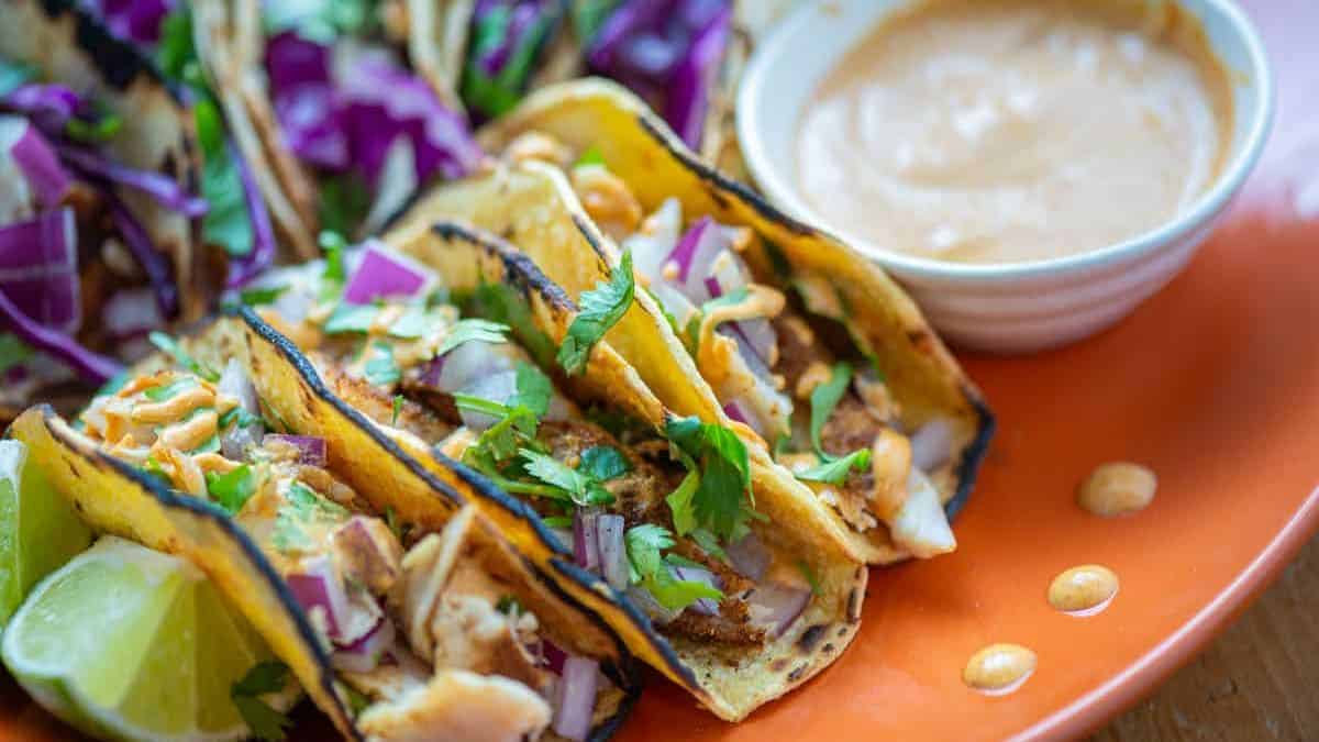 A close-up shot of three pieces of fish tacos served on a plate with some dip on the side. 