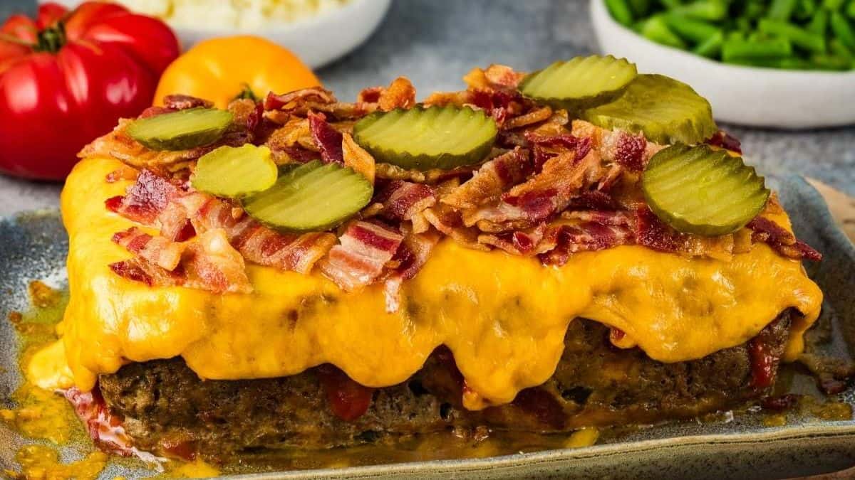 Bacon Cheeseburger Meatloaf topped with cheese, bacon bits and slices of pickles, all set on a baking sheet.