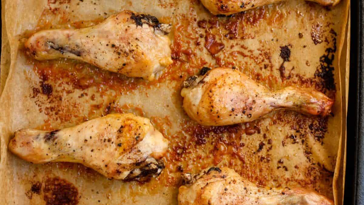 A top shot of a baking tray with baking sheet and some baked chicken thighs. 