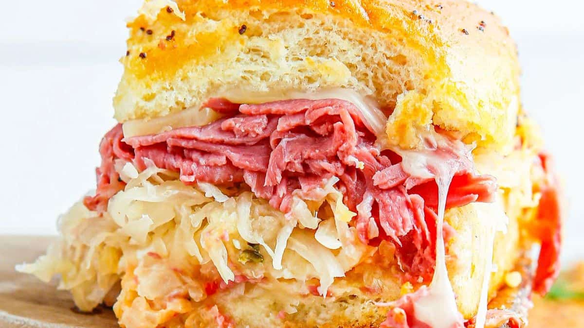 Baked Reuben sliders with corned beef, Swiss cheese and sauerkraut on mini buns.
