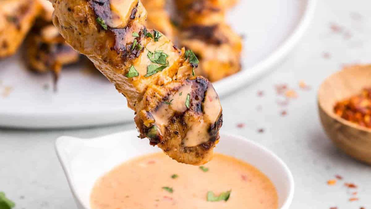 Bang bang chicken skewers with spicy creamy sauce drizzled over grilled chicken pieces.
