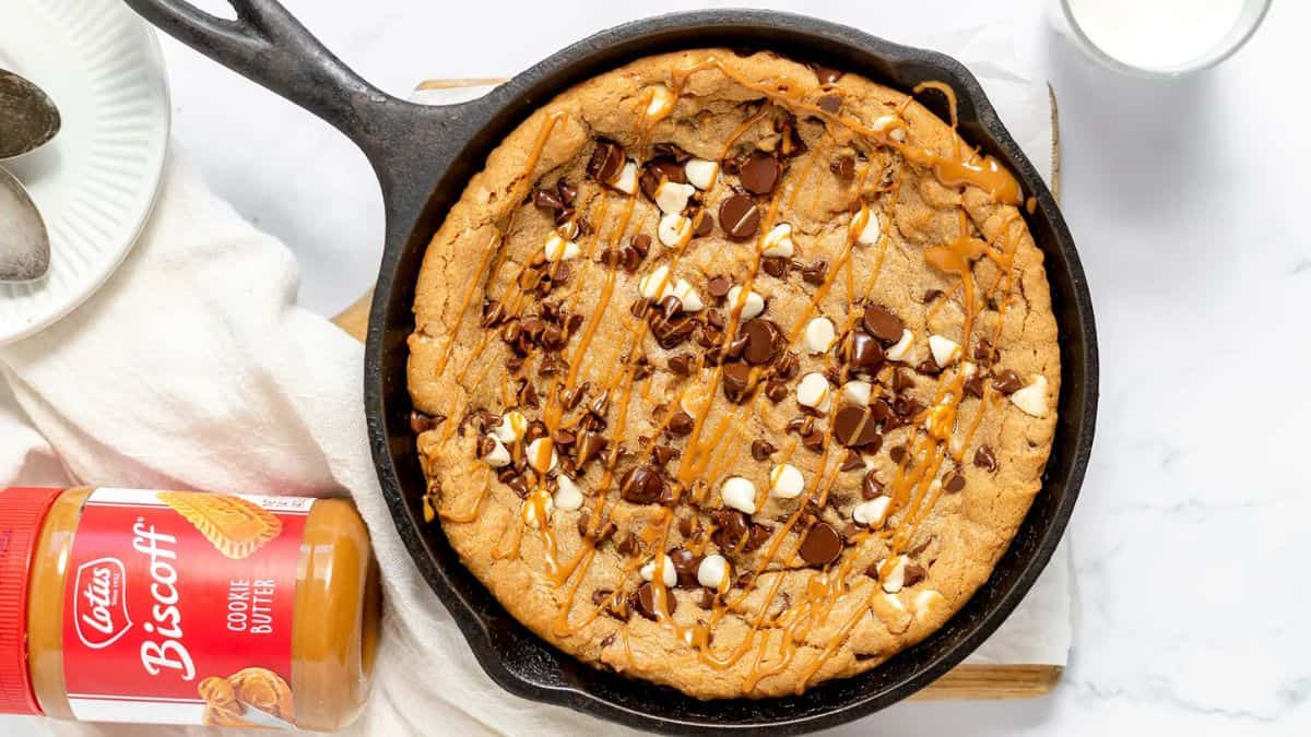 Cookie Butter skillet on a cast iron pan, drizzled with caramel, a jar of biscoff cookie butter can be seen from the side. 