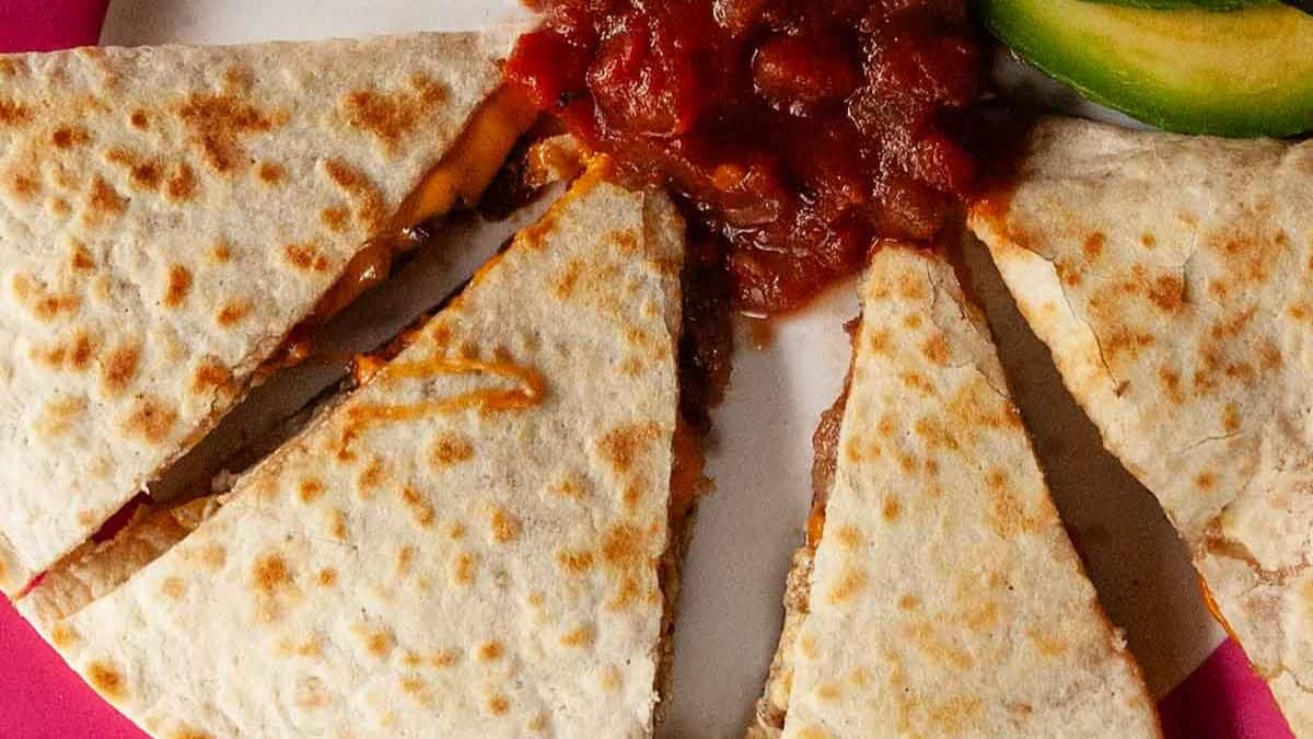 Close-up shot of four pieces of breakfast quesadilla set on a plate, with a salsa dip sauce. 