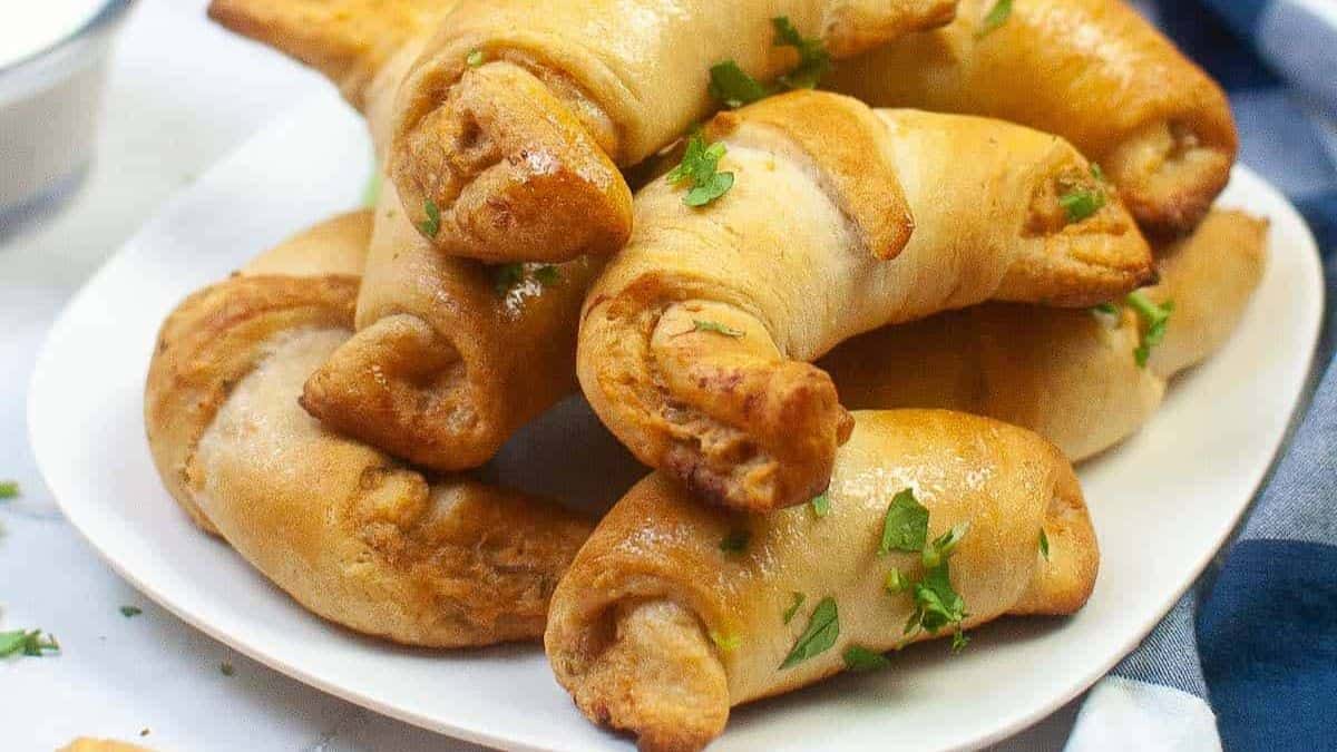 Baked buffalo chicken crescent rolls on a tray, stuffed with spicy shredded chicken and served with celery sticks and dipping sauce.