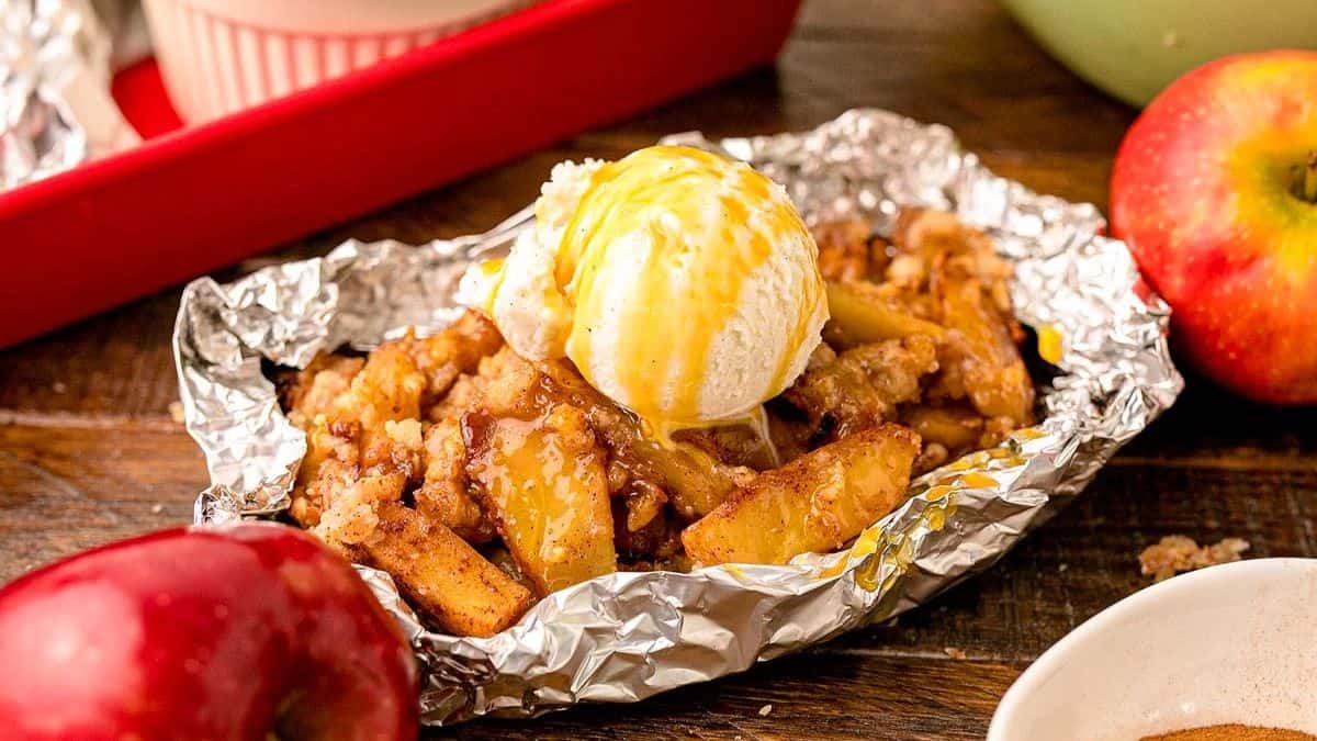 Apple crisps sitting on a aluminum foil, topped with a scoop of vanilla then drizzled with caramel syrup.