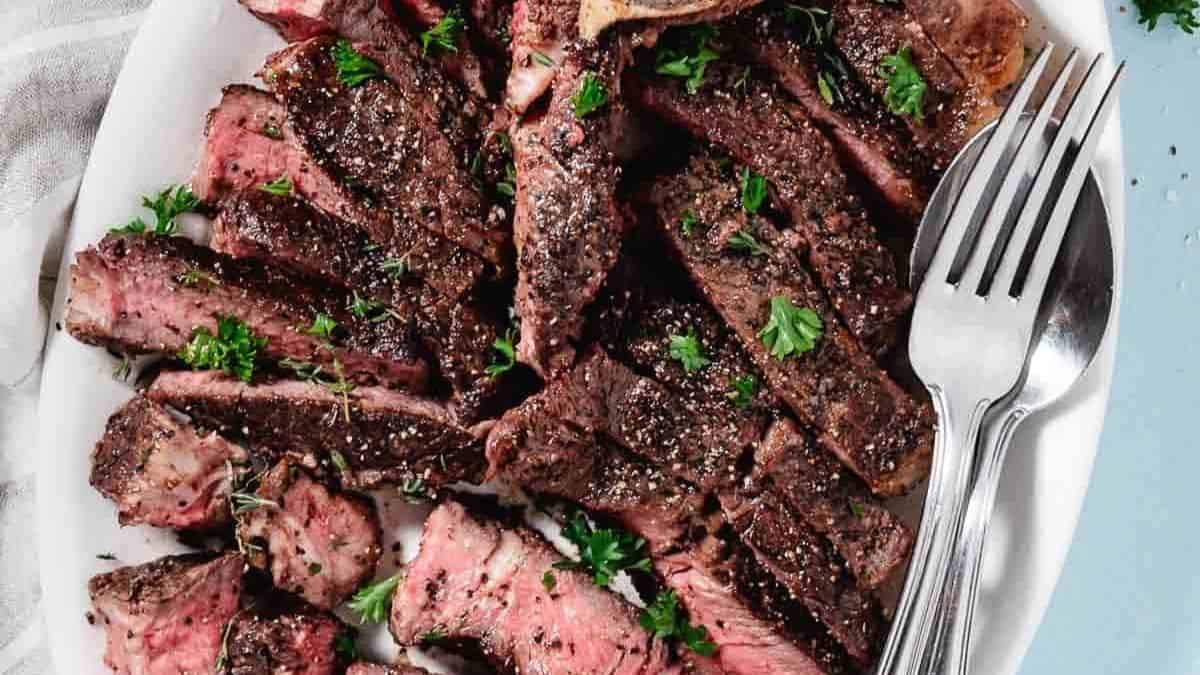 Porterhouse Steak sliced into small pieces set on a platter, a spoon and fork can be seen on the side. 