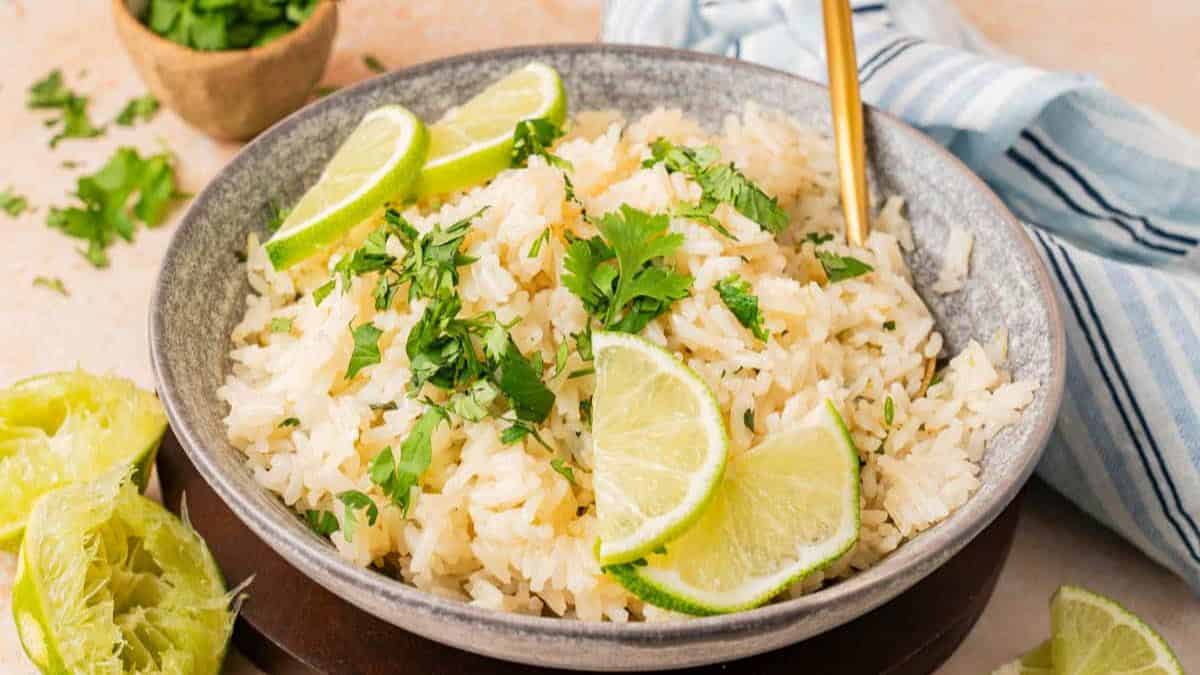 A bowl of Cilantro Rice, with slices of lime, and some cilantro leaves.