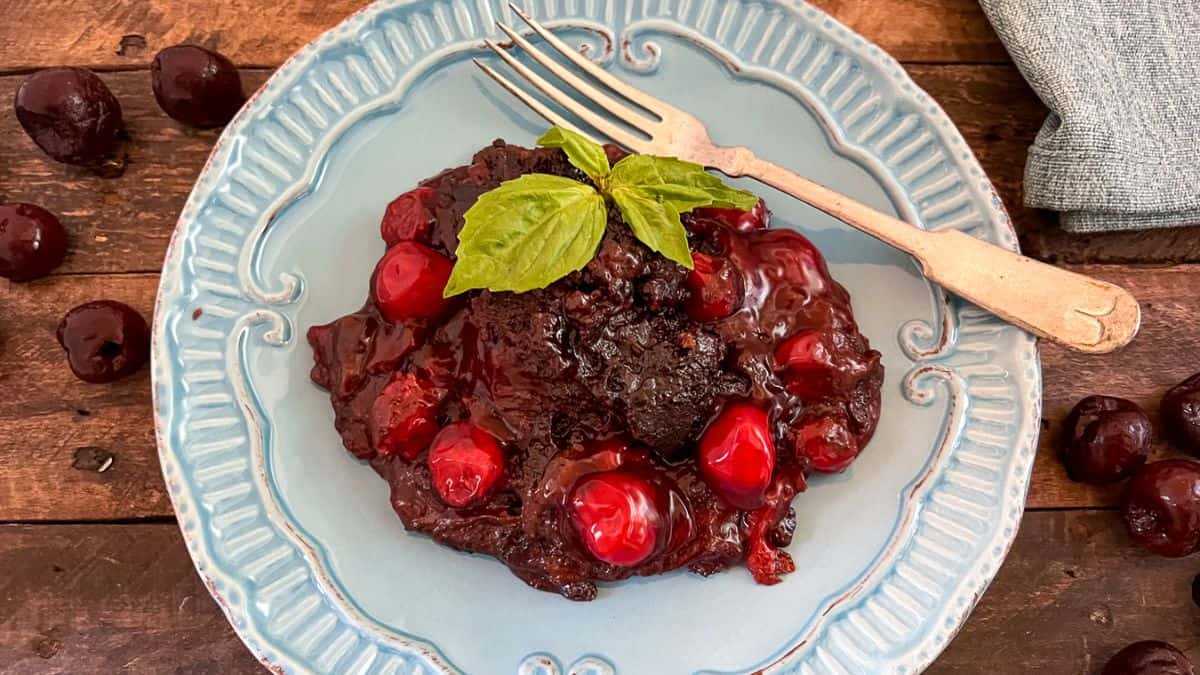 A serving of Cola Chocolate Cherry Cake set on blue plate with a fork on the side.