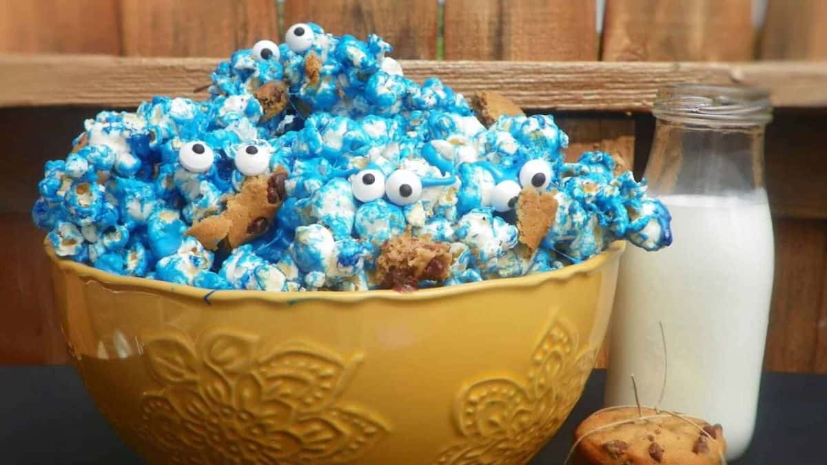 A bowl filled with cookie monster themed popcorn, a bottle of milk on the side.