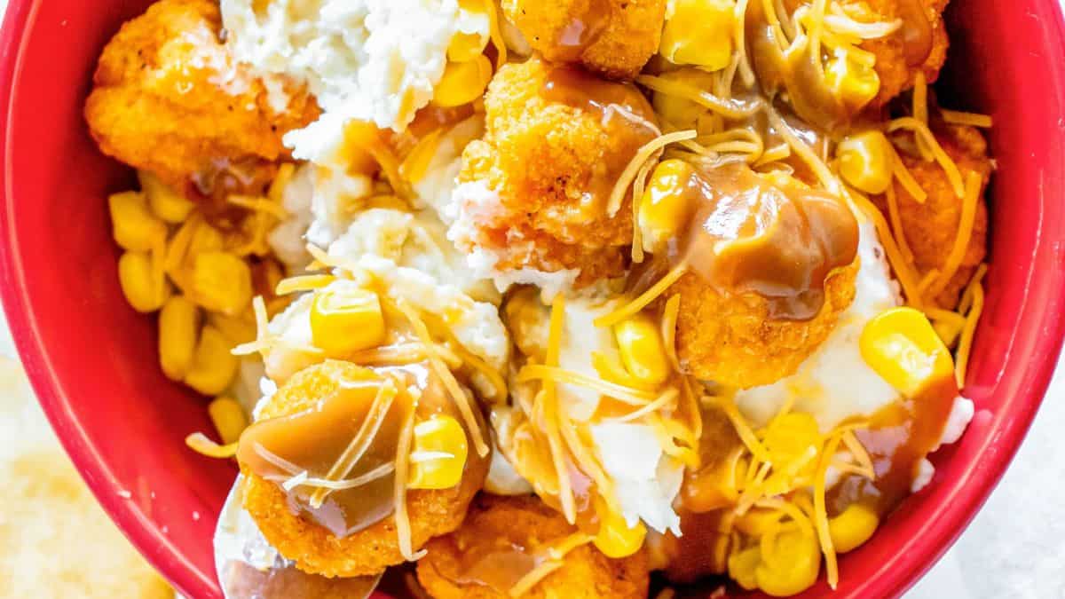 Close-up shot of a bowl filled with chicken popcorn, mashed potatoes, cheese, and some bits of kernel corn. 
