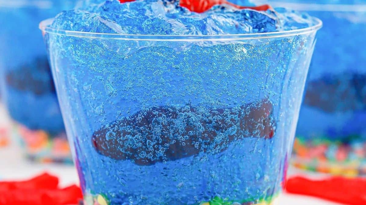 A close-up shot of a clear cup with blue gelatin and fish candies.