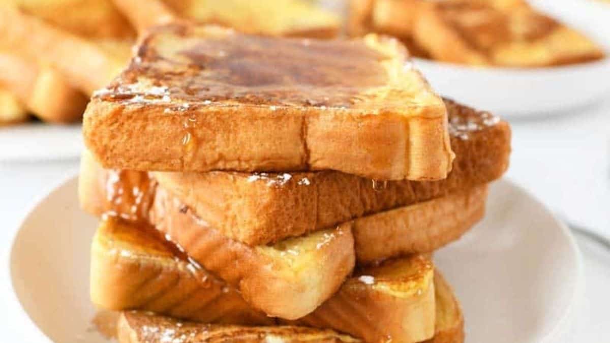 A stack of French toast set on a plate with drizzle of maple syrup.