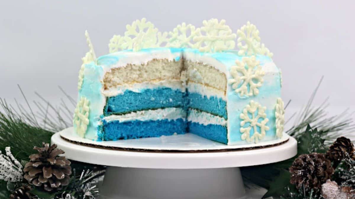 Three-layer Frozen themed cake cut in the middle, that laid on top of a cake stand.
