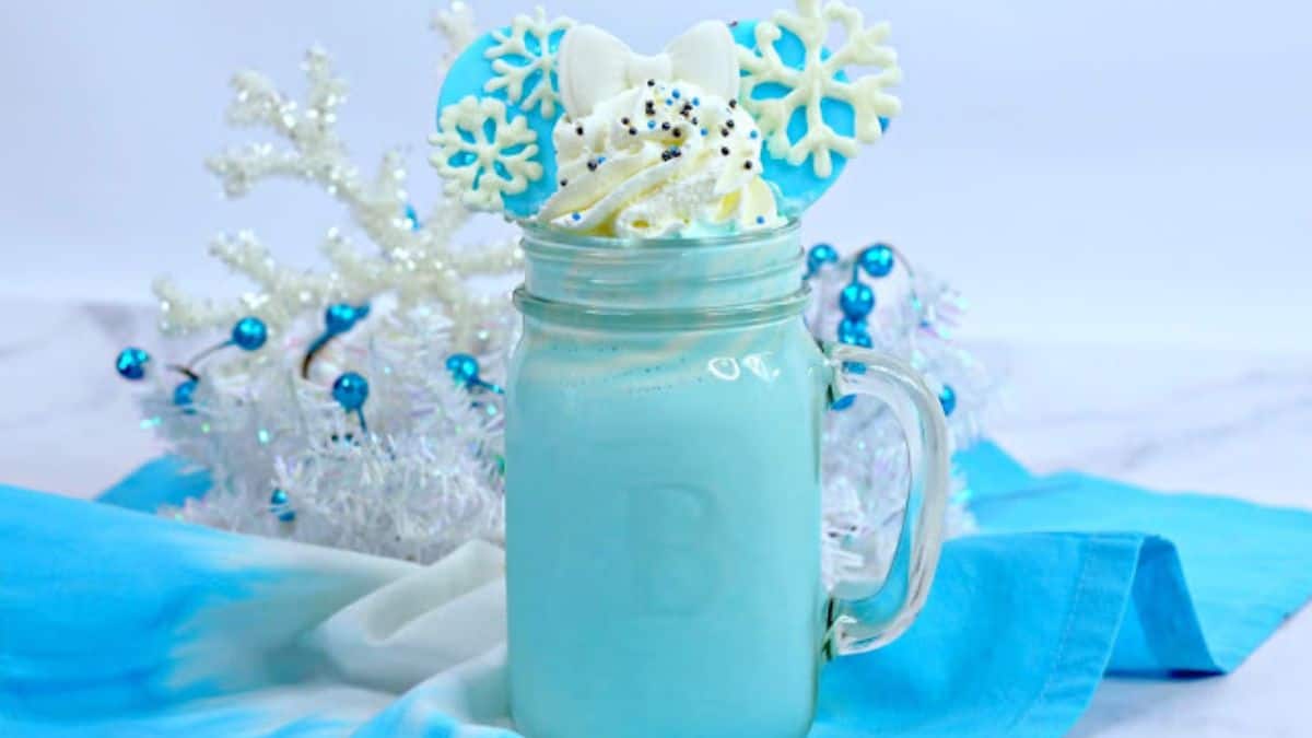 A mason jar with light blue colored hot chocolate topped with whipped cream.