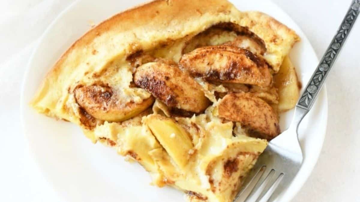 A serving of pancakes with slices of apples set on a plate with a fork. 