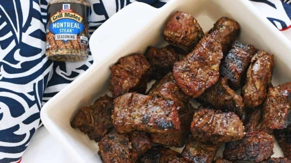 Small chunks of grilled steak on a serving dish and a bottle of seasoning on the side. 