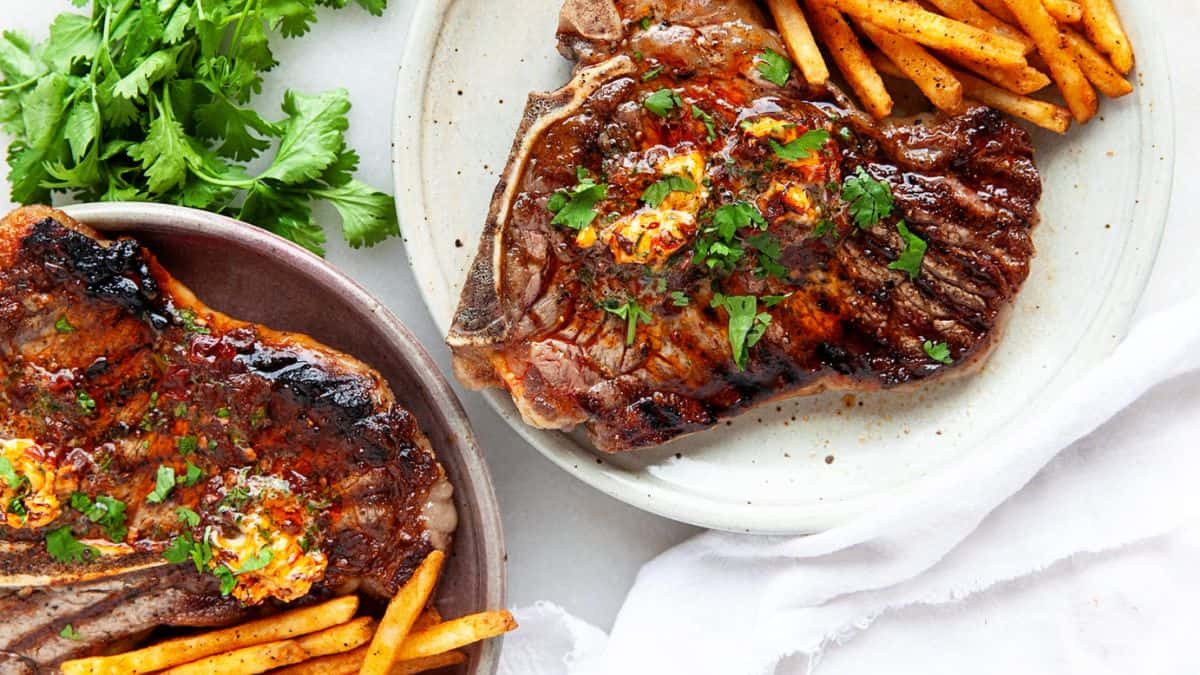 Two plates with grilled T-bone steak and fries each. 