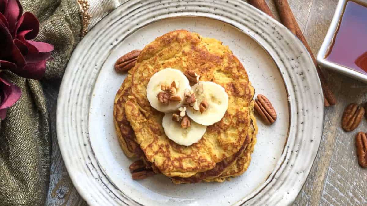 Top shot of a pancake stack set on a plate then topped with chopped pecans and slices of banana. 