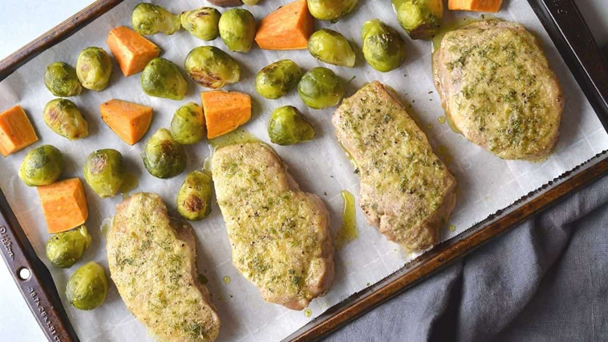 Four pieces of porkchop cutlets and a couple pieces of brussels sprout and potatoes and all set on a baking tray lined with parchment. 