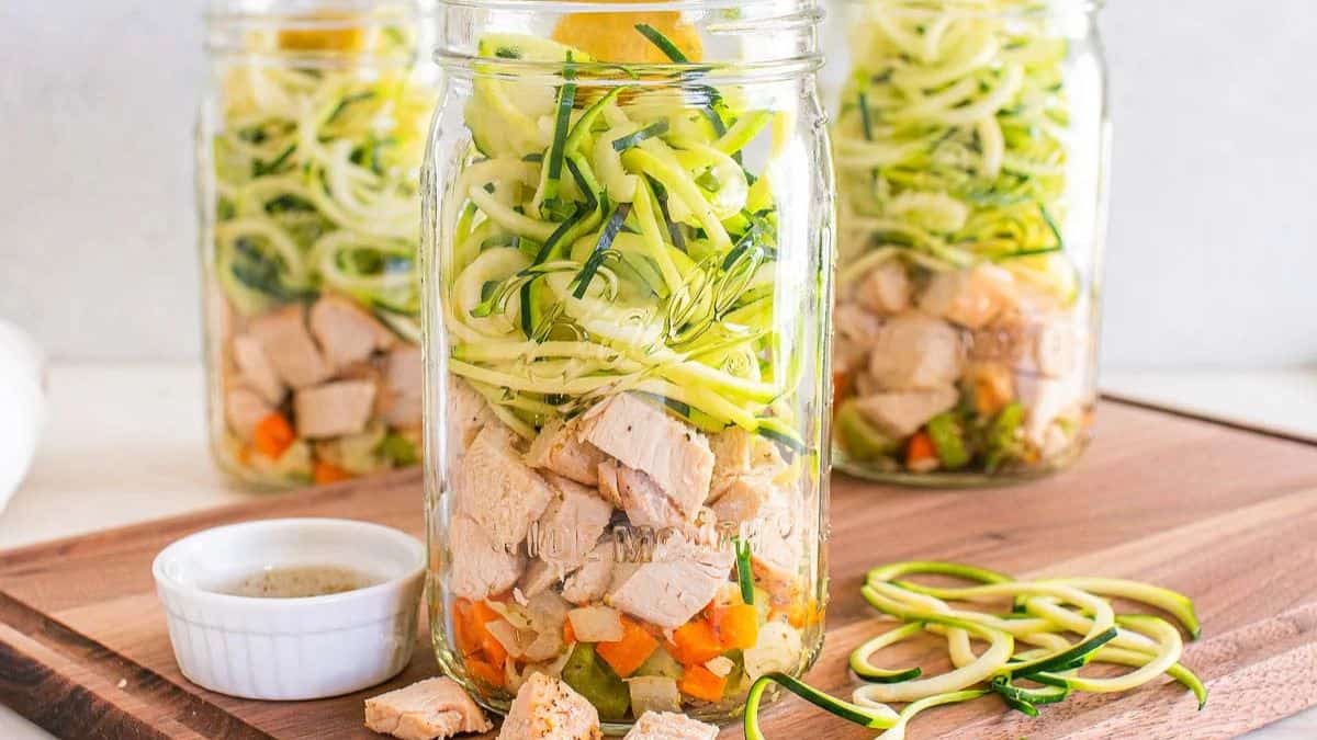 Mason jar brimming with layered chicken, zucchini noodles, and vegetables for chicken zoodle soup mix.