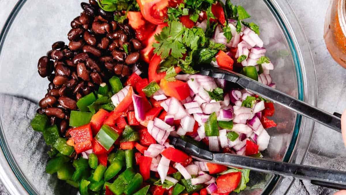 A clear bowl filled with chopped onion, tomatoes, green peppers, cilantros, and beans.
