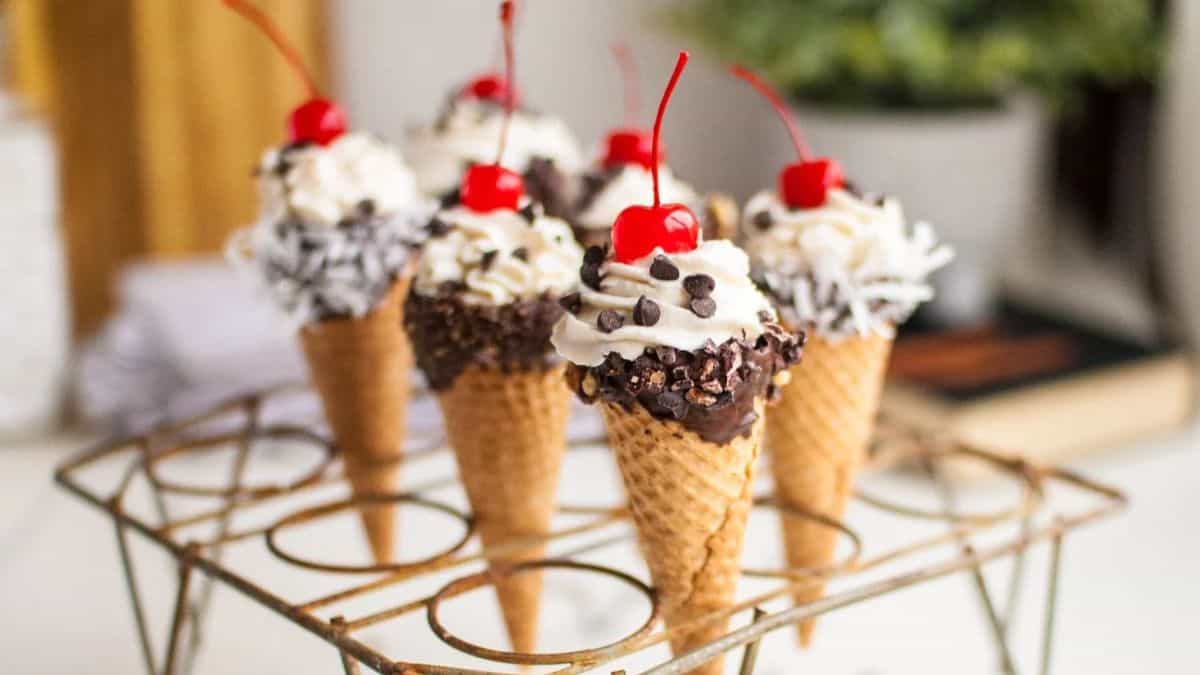 Six pieces of cones with cream topped with cherries and small chocolate pieces. 