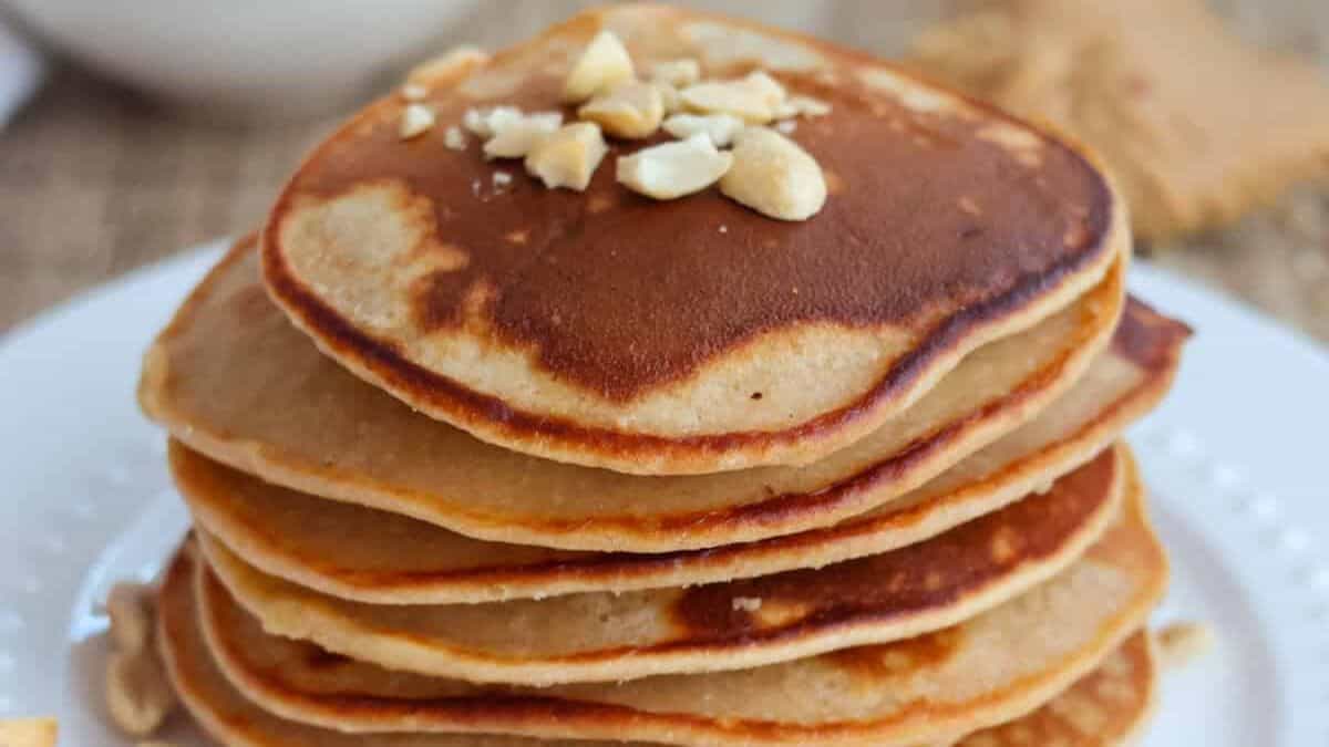 A stack of pancakes set on a plate, topped with crushed peanuts. 