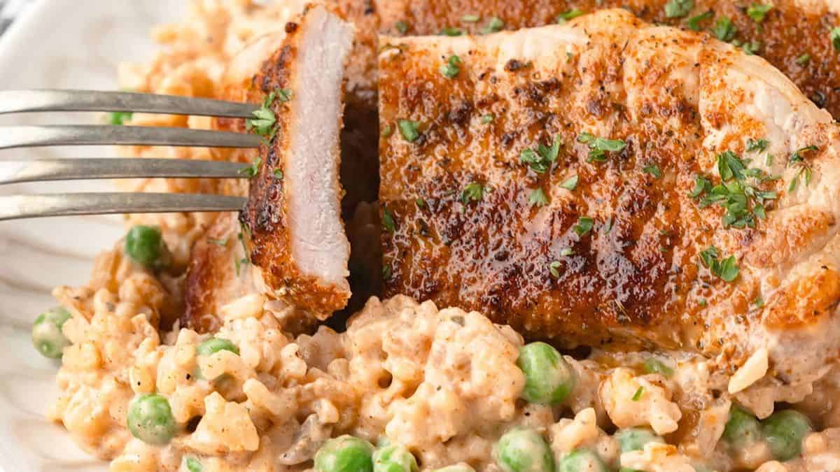 A close up shot of a sliced porkchop sitting on a bed of rice with peas. 