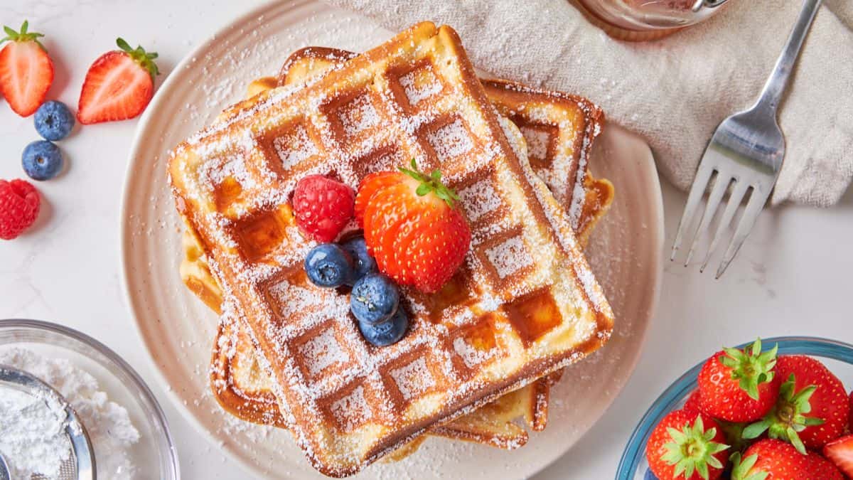 Top shot of stack of waffles topped with strawberries, blueberries, raspberries that is then set on a plate.