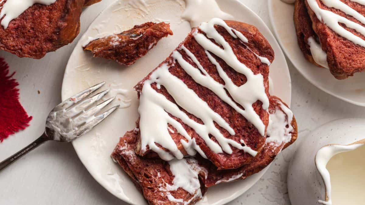 Top shot of a plate with Red Velvet French Toast drizzled with Cream Cheese sauce then was cut with a fork. 