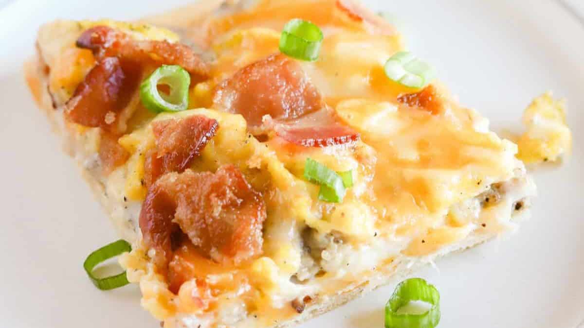 Square breakfast pizza with a flaky crescent roll crust topped with creamy sausage gravy, scrambled eggs, bacon, and melted cheese.