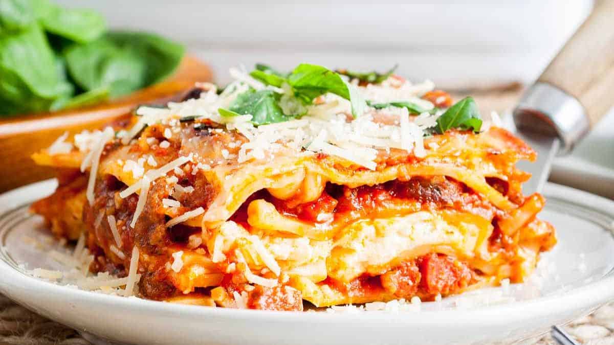 One serving of Pepperoni Lasagna set on a plate topped with cheese and some basil leaves. 