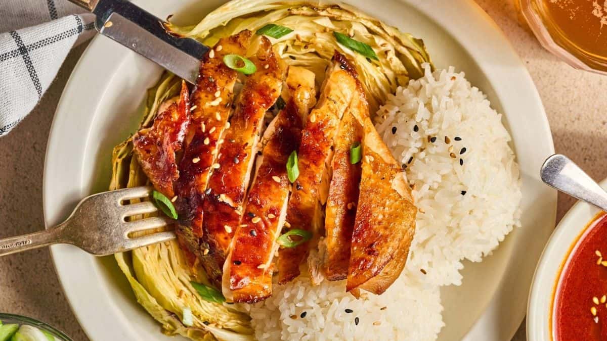 A plate with baked gochujang chicken and cabbage with steamed rice on the side.