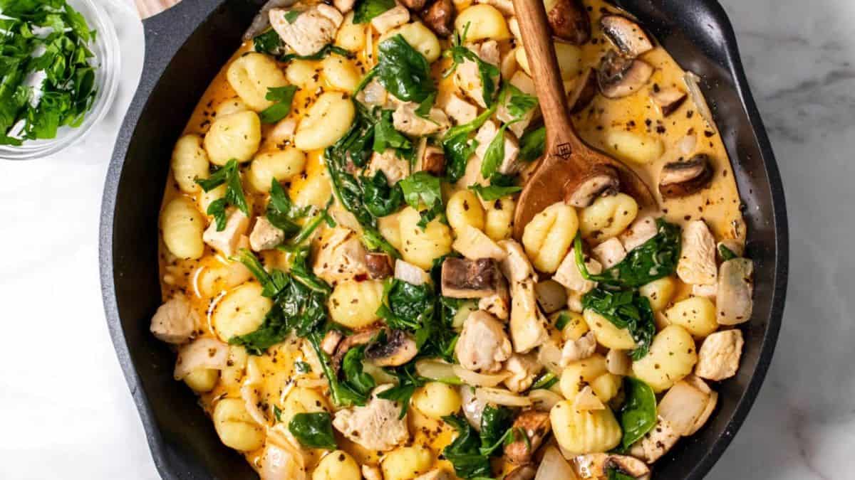 Chicken and gnocchi dish in a skillet with a wooden ladle. 