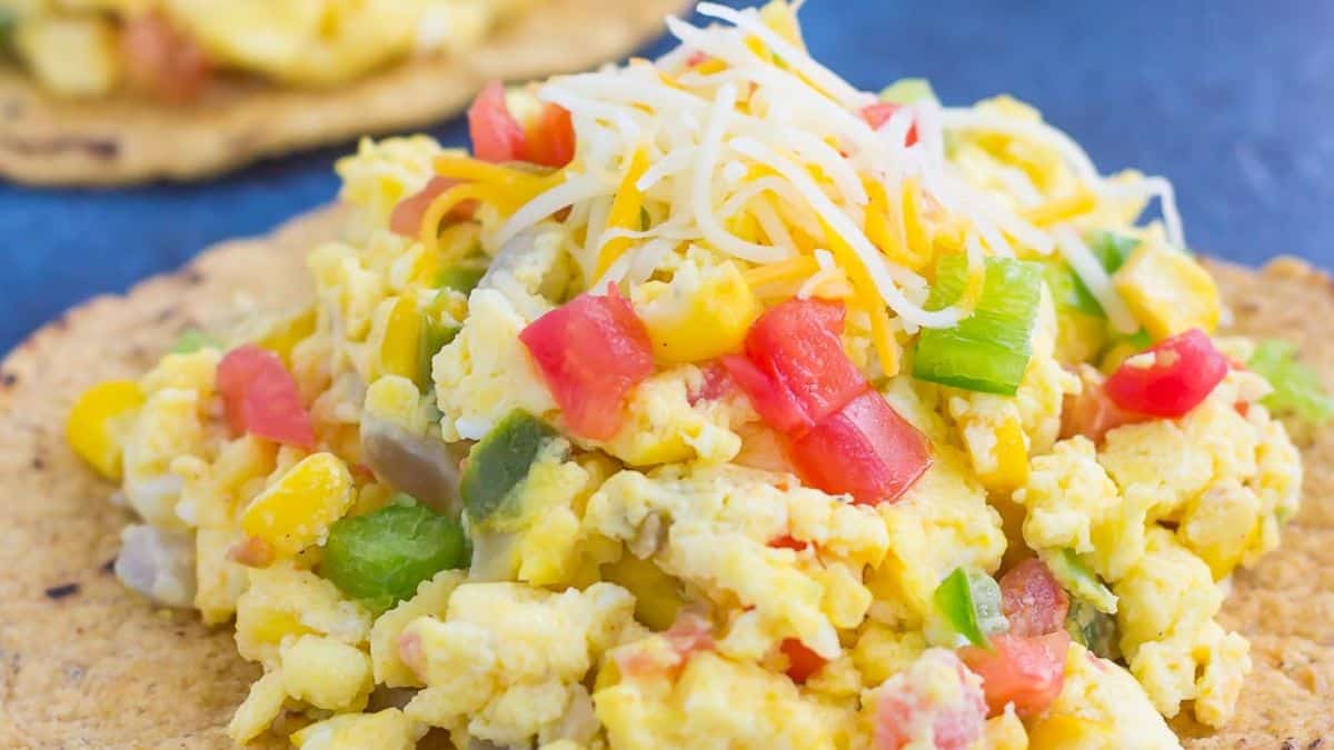A close-up shot of a southwest scramble tostada with chops of red and green peppers, and shredded cheese on top. 